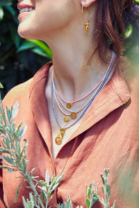 Emily Koliandri is wearing a combo of 5 different necklaces with miyuki beads, silver 925 gold plated chain and silver 925 gold plated charms in various shapes. Also is wearing a silver 925 gold plated earring with a silver 925 gold plated triangle charm with a palm tree.