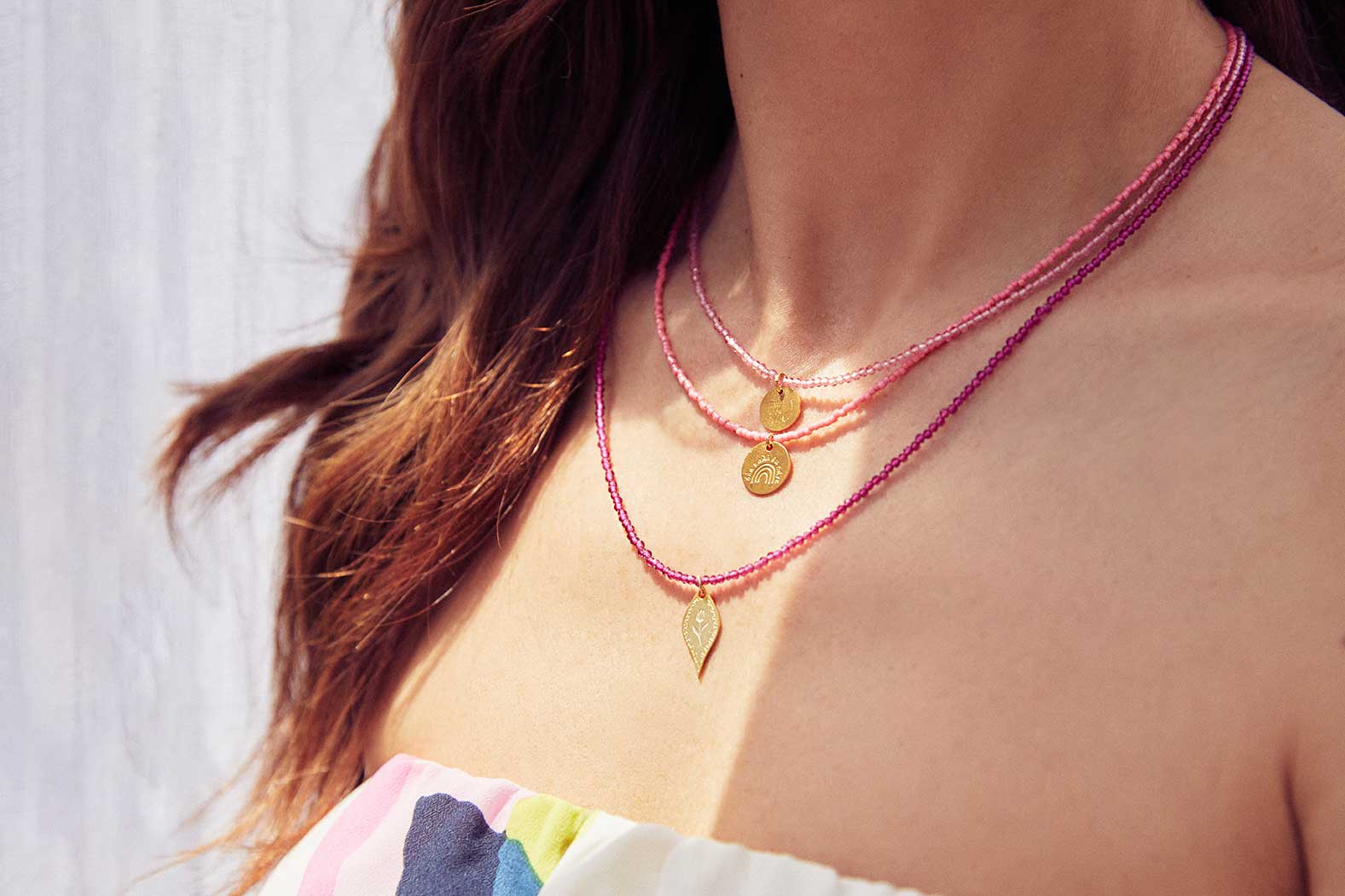 Emily Koliandri is wearing a combo in fucshia tones of 3 different necklaces with miyuki beads, semiprecious stones combined with silver 925 gold plated charms in various shapes.