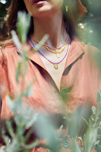 Emily Koliandri in her yard is wearing 3 necklaces made with semiprecious stones, miyuki beads and silver 925 gold plated charms with different messages.